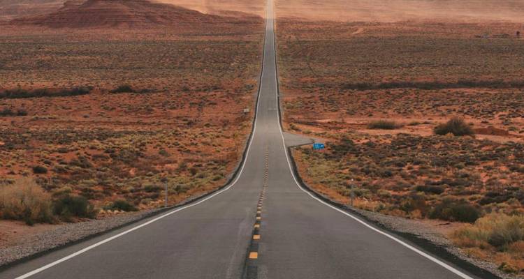 Una carretera interminable y recta te lleva hacia mesetas rojas atravesando un desierto árido en Monument Valley.