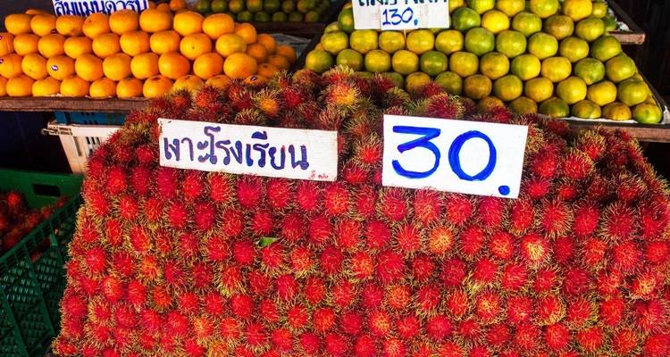 Des piles de ramboutan d'un rouge éclatant exposées dans un marché de fruits thaïlandais avec des panneaux de prix écrits à la main.