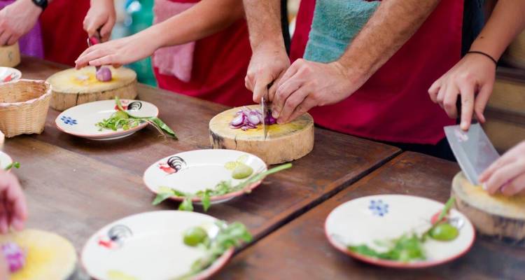 Les participants à un cours de cuisine thaïlandaise tranchent les ingrédients sur de petites planches en bois à une table commune.