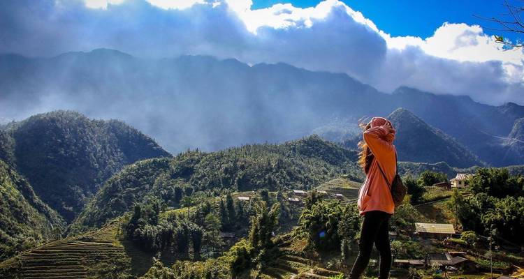 Femme profitant d'une vue panoramique sur des champs en terrasses et des montagnes avec un ciel dramatique.