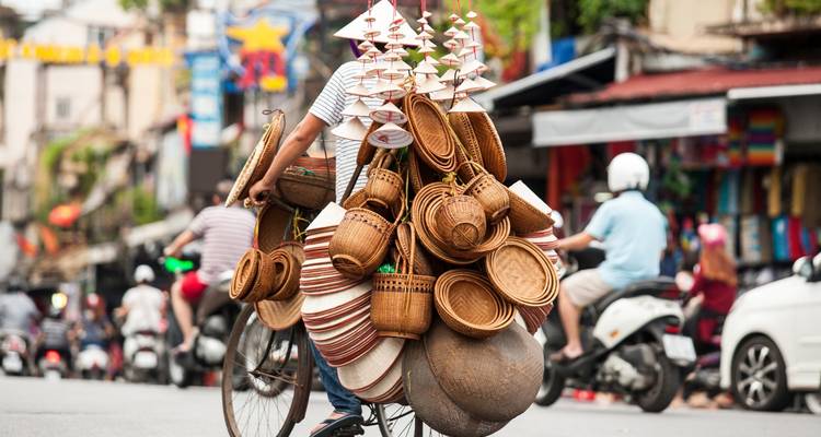 Vendor on bicycle with baskets in street.