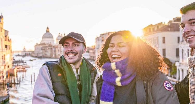 Happy friends stand on a bridge over Venice's Grand Canal with evening sun shining behind them