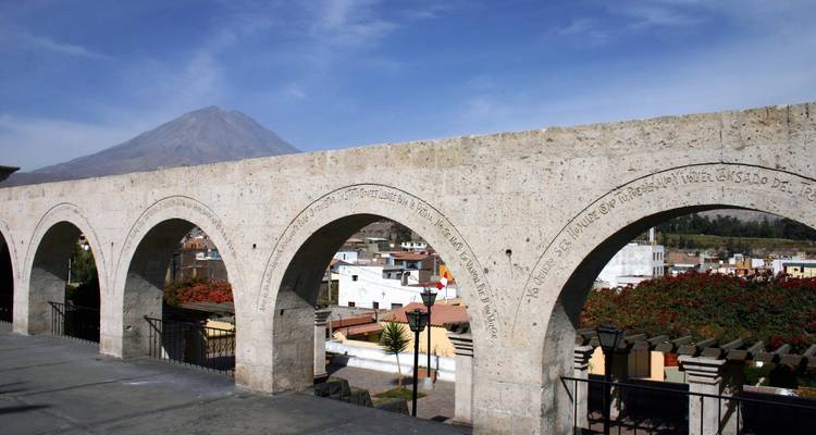 Terrasse voûtée surplombant une ville avec un volcan au loin.