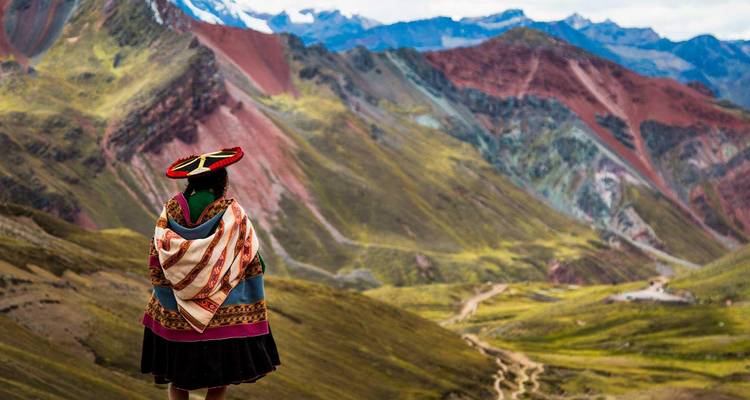 Persona en atuendo tradicional contemplando colinas coloridas.