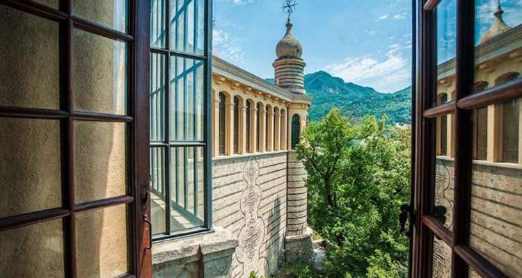 Uitzicht vanuit een raam met een historisch gebouw en bergen in de verte.