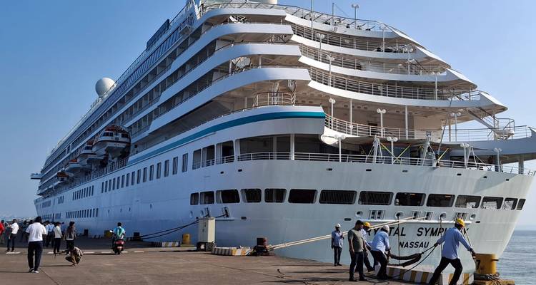 Large cruise ship docked at port with workers on the pier