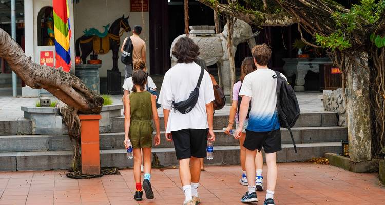Visitantes vestidos de manera casual caminan hacia la entrada de un complejo de templos histórico con banderas coloridas.