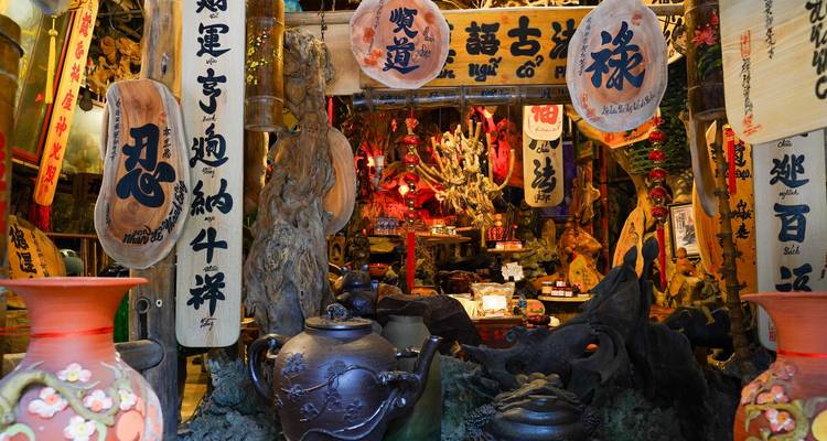 Tienda de curiosidades abarrotada llena de paneles de caligrafía, teteras y decoraciones tradicionales bajo luz cálida.