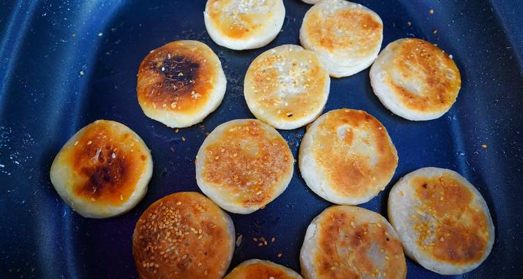 Las empanadas doradas de sésamo chisporrotean sobre la superficie oscura de una sartén.
