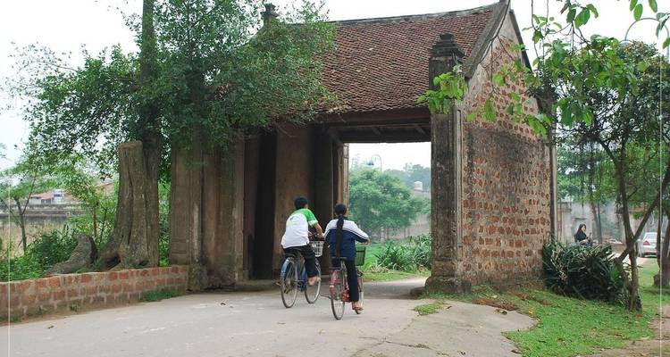 Two cyclists ride through an ancient brick gate of a traditional Vietnamese village
