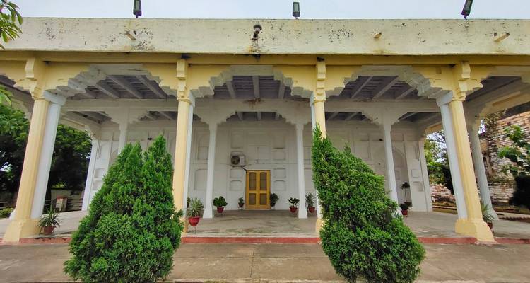 Eenvoudig koloniaal gebouw met potplanten bij de ingang.