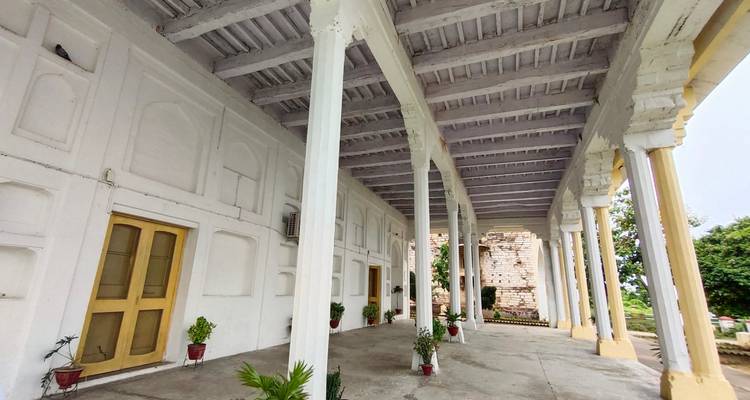 Wit gebouw met bogen en potplanten onder een bewolkte hemel.