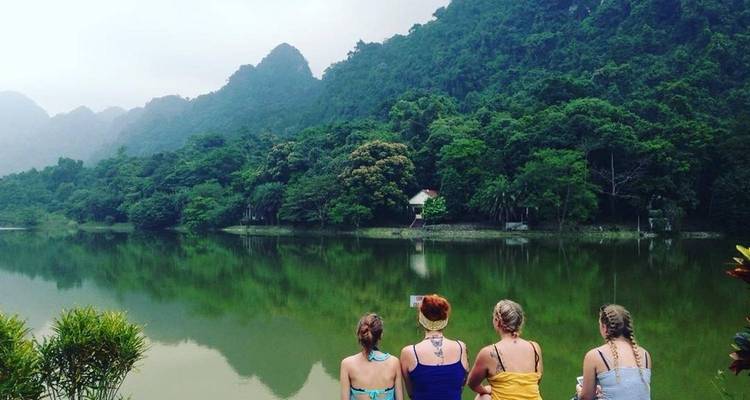 Vier Frauen sitzen an einem stillen See und fotografieren die üppigen bewaldeten Hügel auf der anderen Seite des Wassers