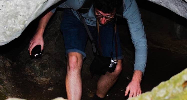 Ein Reisender hockt sich hin und zwängt sich durch eine niedrige Höhlenöffnung, wobei er eine Taschenlampe benutzt, um den felsigen Durchgang zu sehen.