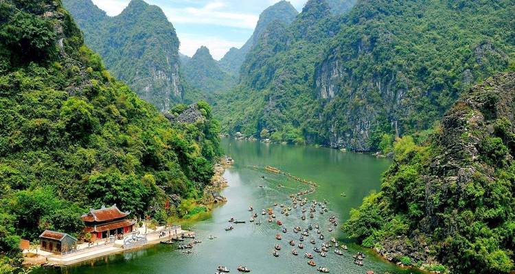 Sweeping aerial of a river canyon with hundreds of small tourist boats and a riverside shrine among karst peaks