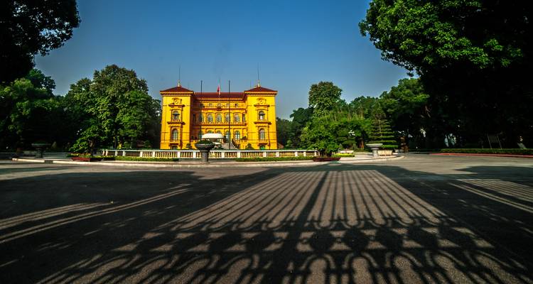Vista frontal del Palacio Presidencial amarillo en Hanói enmarcado por sombras ornamentadas de hierro forjado