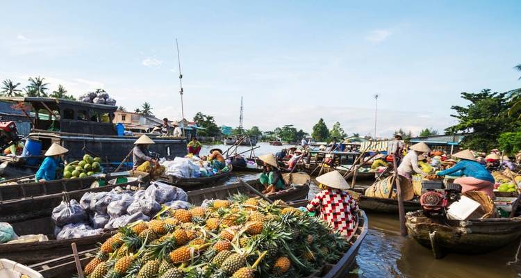 Bustling scene of boats packed with pineapples and other produce trading on a busy Mekong floating market.