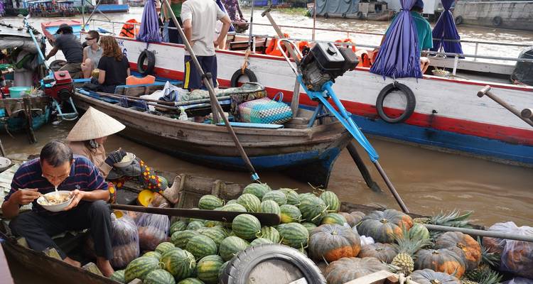 Longtail boats laden with watermelons and pumpkins crowd a muddy river market.