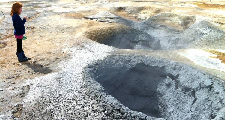 Geothermisch gebied met stoom die oprijst uit hete bronnen en een persoon die toekijkt.