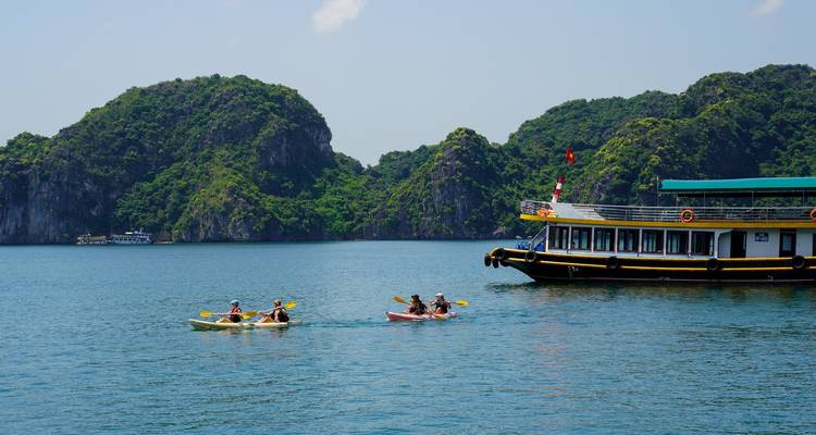 Los kayakistas reman cerca de un crucero entre exuberantes acantilados de piedra caliza en un día soleado.