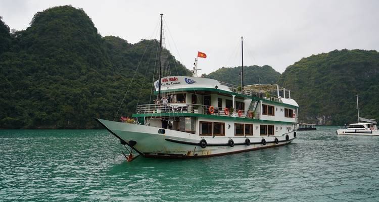 Barco de crucero nocturno blanco y verde anclado en aguas color jade contra altos acantilados kársticos.