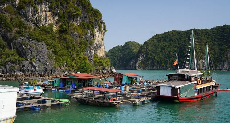 Aldea pesquera flotante y embarcaciones enclavadas junto a espectaculares acantilados de piedra caliza en aguas color esmeralda.