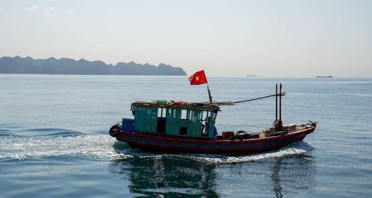 Pequeño bote de pesca de madera con bandera vietnamita acelera a través del mar azul tranquilo.