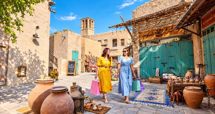 Deux acheteuses élégantes transportant des sacs colorés à travers les ruelles restaurées du quartier historique Al Fahidi de Dubaï.