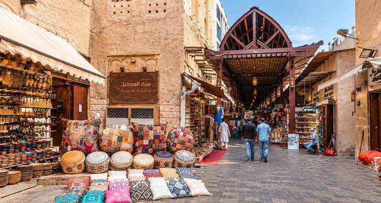 Ruelle colorée du souk bordée de textiles, d'épices et de lanternes dans le Vieux Dubaï avec des acheteurs en train de parcourir les étalages.