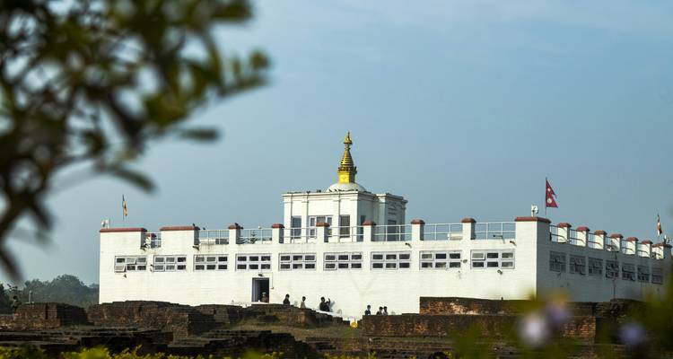 Der weiße Maya Devi Tempel in Lumbini erhebt sich gegen einen blauen Himmel mit Pilgern darunter.