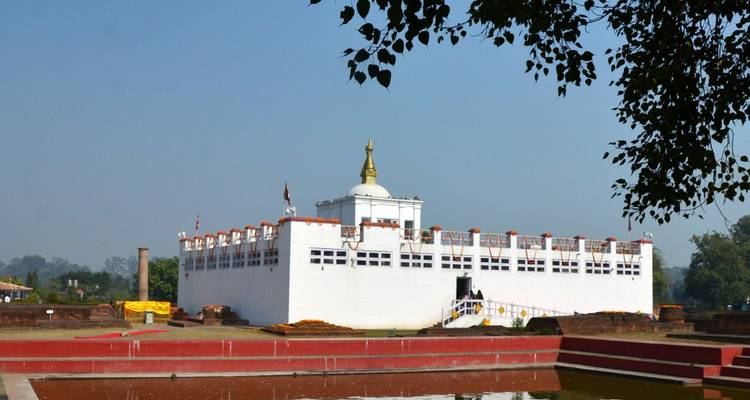 Der weiße Maya Devi Temple steht in einer ruhigen Anlage unter einem klaren blauen Himmel.