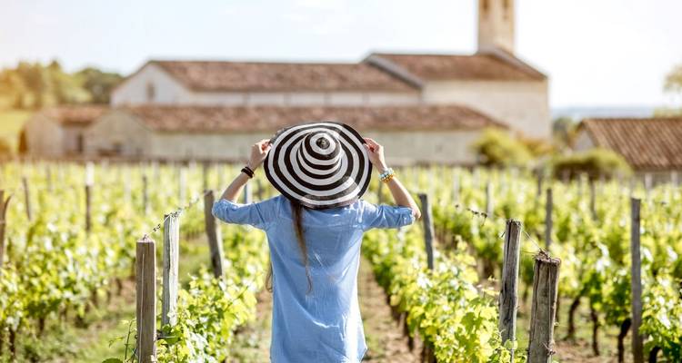 Personne avec un chapeau debout dans un vignoble avec une église en arrière-plan.