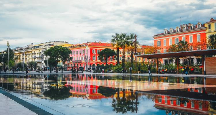 Bâtiments colorés se reflétant dans un miroir d'eau sur une place de ville.