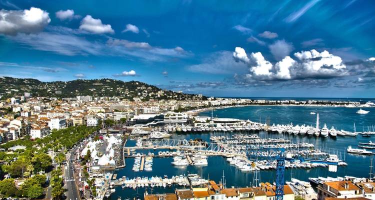 Marina avec yachts et ville côtière sous un ciel lumineux.