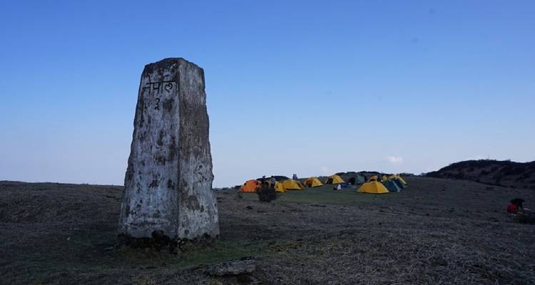 Steinmarkierung auf einem Hügel mit Zelten im Hintergrund.