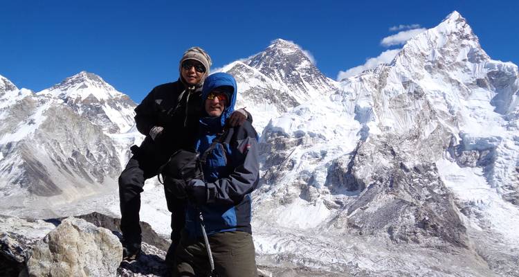 Zwei Kletterer, die auf einem felsigen Gipfel posieren, mit schneebedeckten Bergen im Hintergrund.