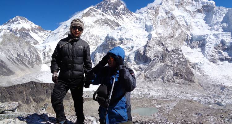 Zwei Wanderer in den Bergen mit einem schneebedeckten Gipfel im Hintergrund.