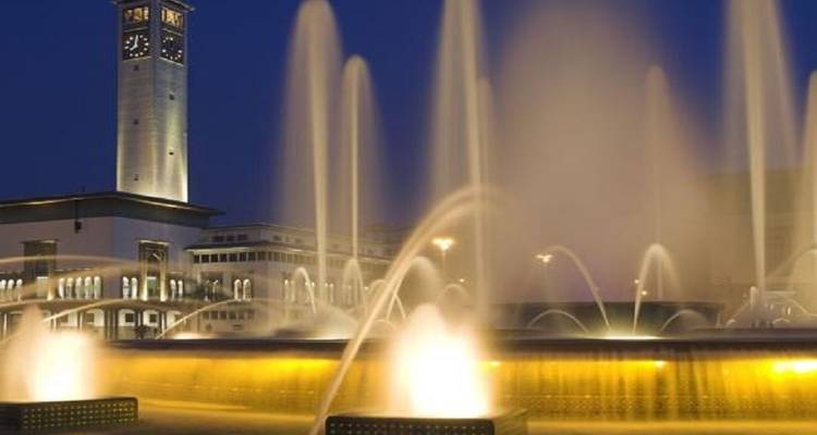 Fountain with colored lights at night with a clock tower.