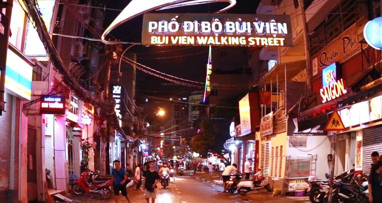 Lebendige Stadtstraße bei Nacht, erleuchtet von Schildern und voller Aktivität