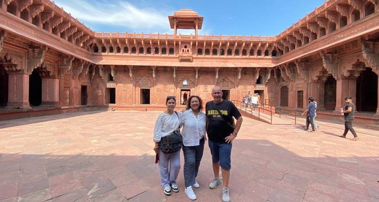 Los viajeros sonríen dentro de un espacioso patio de arenisca roja con arcos ornamentados