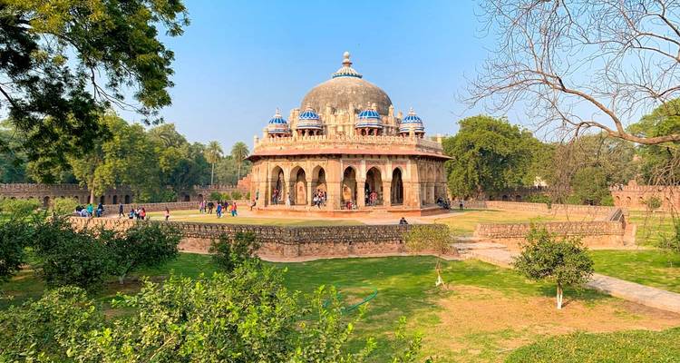 Tumba histórica con cúpula situada en jardines exuberantes con visitantes explorando los senderos