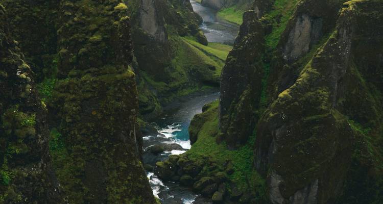 Tiefe Schlucht mit einem fließenden Fluss, umgeben von hoch aufragenden grünen Klippen.
