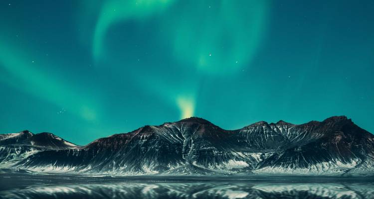 Les spectaculaires tourbillons verts de l'aurore boréale s'étirent au-dessus d'une chaîne montagneuse saupoudrée de neige sous un ciel étoilé.