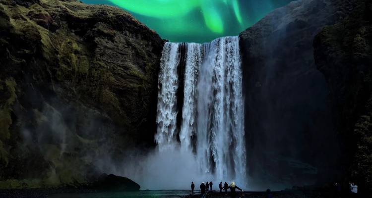 La cascade de Skógafoss gronde dans l'obscurité tandis que les aurores boréales aux couleurs éclatantes dansent à travers le ciel.