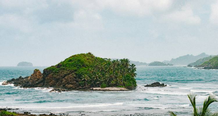 Île rocheuse isolée couverte de végétation, entourée par l'océan.