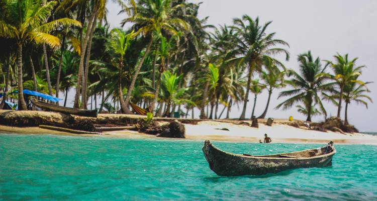 Bateau traditionnel en bois près d'une plage bordée de palmiers.
