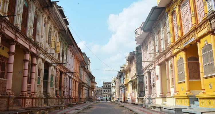 Una calle colonial desierta bordeada de edificios ornamentados en rosa pastel y amarillo bajo un cielo azul brillante.