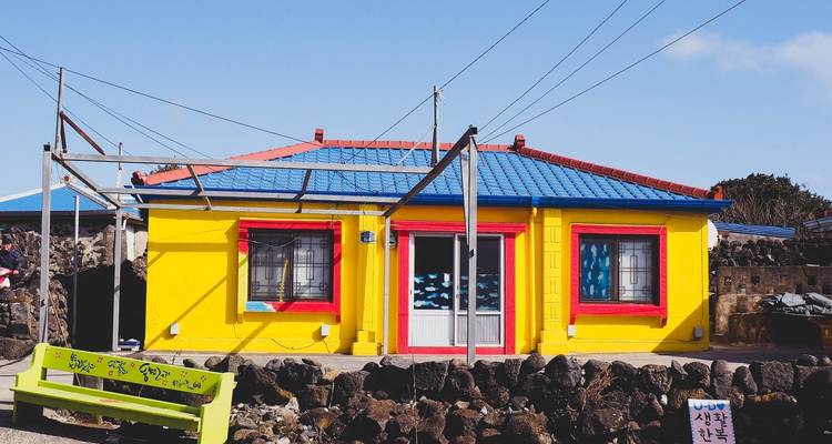 Une maison aux couleurs vives avec une façade jaune et un toit bleu, entourée de rochers.
