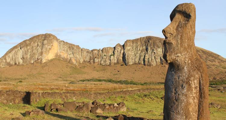 Estatua moai con acantilados rocosos al fondo al atardecer.