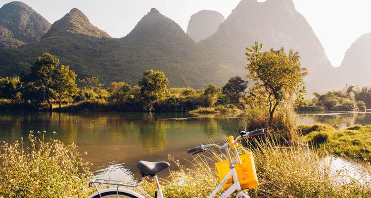 Paisaje escénico con una bicicleta cerca de un río, y montañas kársticas en el fondo.